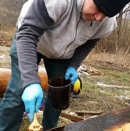 Mężczyzna smaruje drewno smolą.